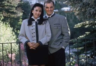 Man and woman standing next to railing, Sonnenalp Hotel in the background