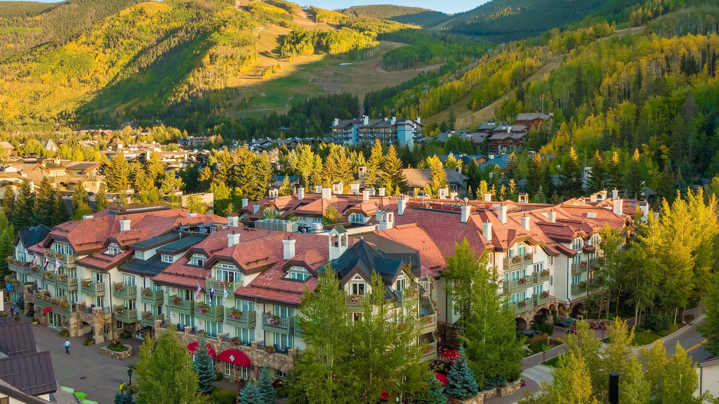 A large building complex with red roofs and white walls surrounded by trees and mountains.