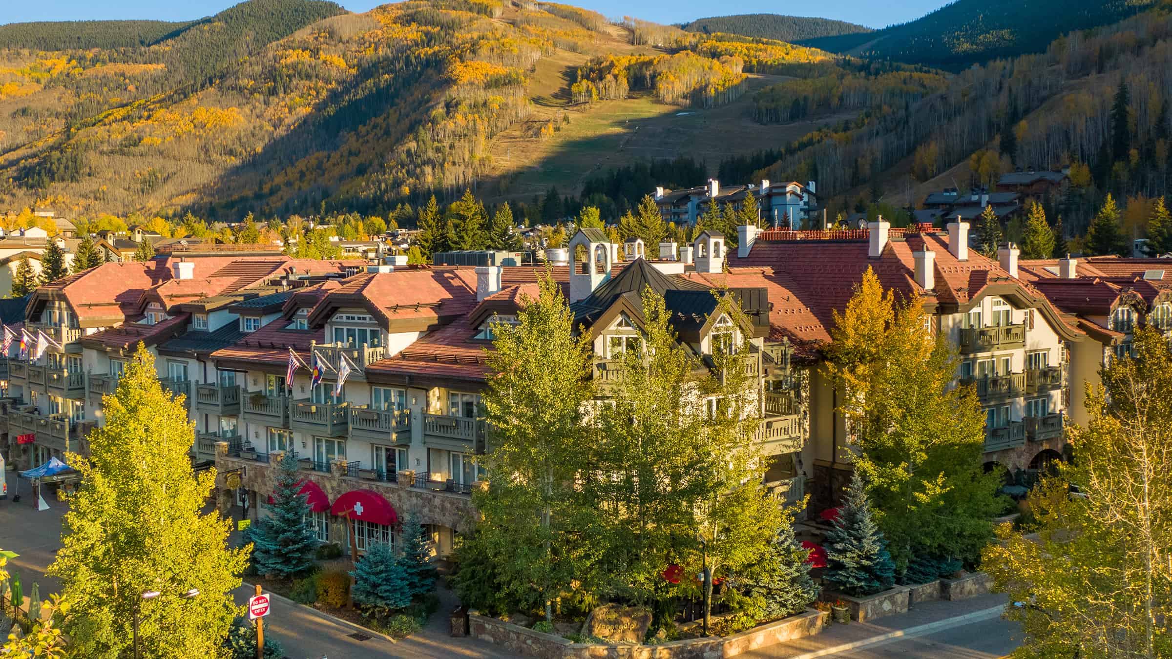 A large building with red roofs and balconies, surrounded by trees and mountains.