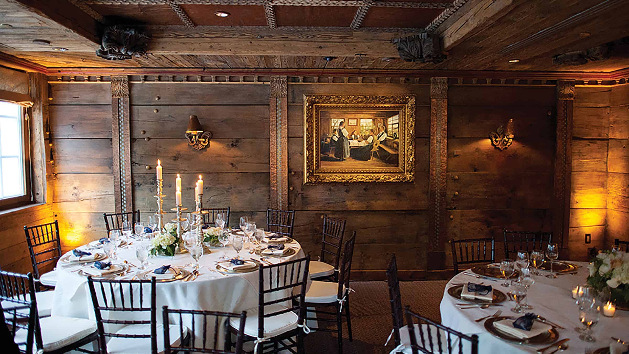 A formal dining room with wooden walls and round tables set for a meal.