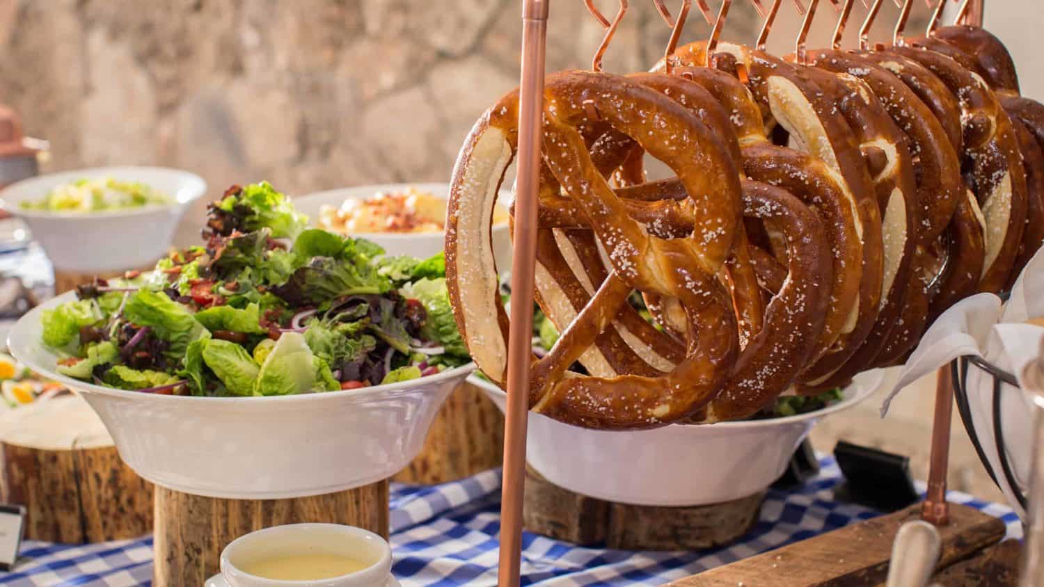 Pretzels hanging from hooks next to salad bowl, other entrees in the background