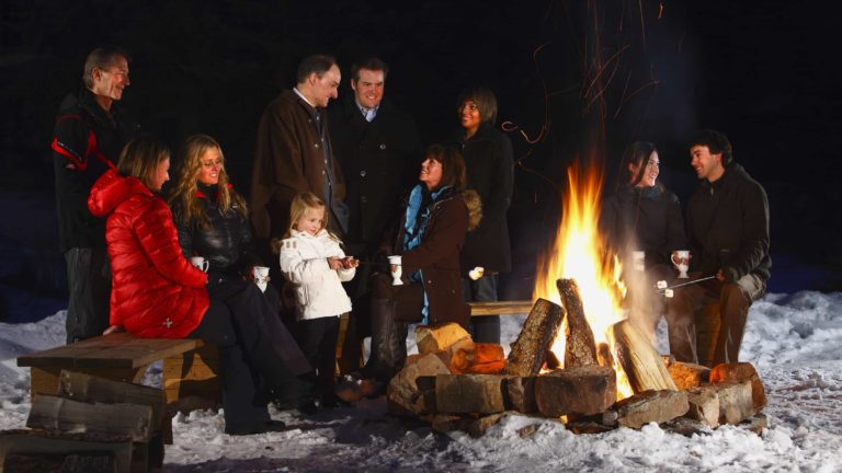 people gathered outdoors next to a firepit, some roasting marshmellows