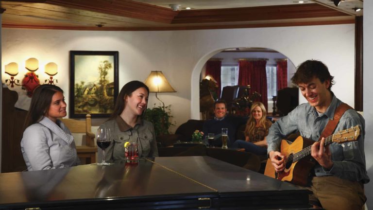 man playing guitar in lounge area as people listen