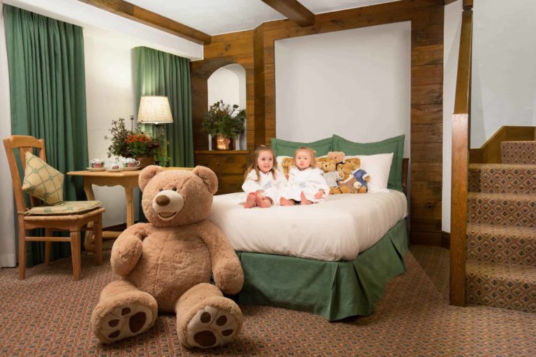 children wearing robes on bed and large teddy bear at the foot of bed