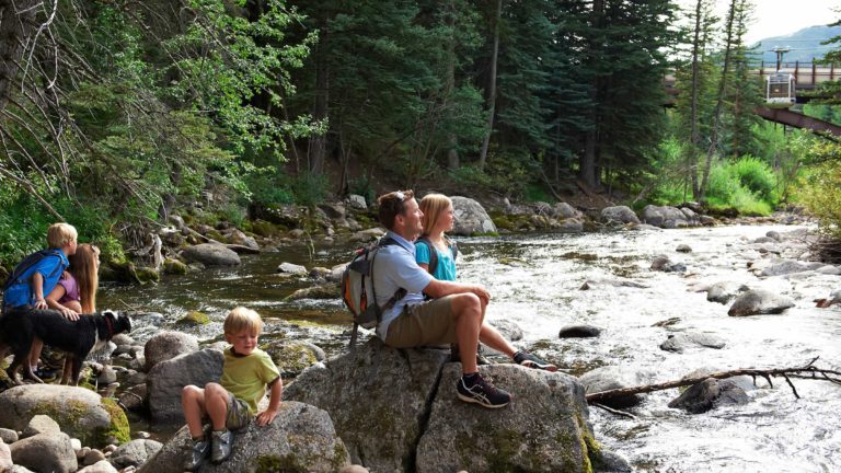 family with dog sitting on rocks on the bank of a creek