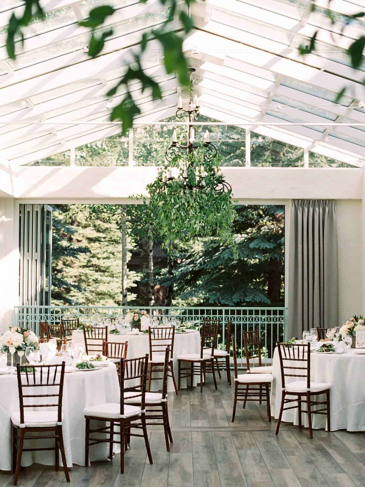 A dining room with round tables set with white tablecloths, chairs, flowers, and a chandelier.