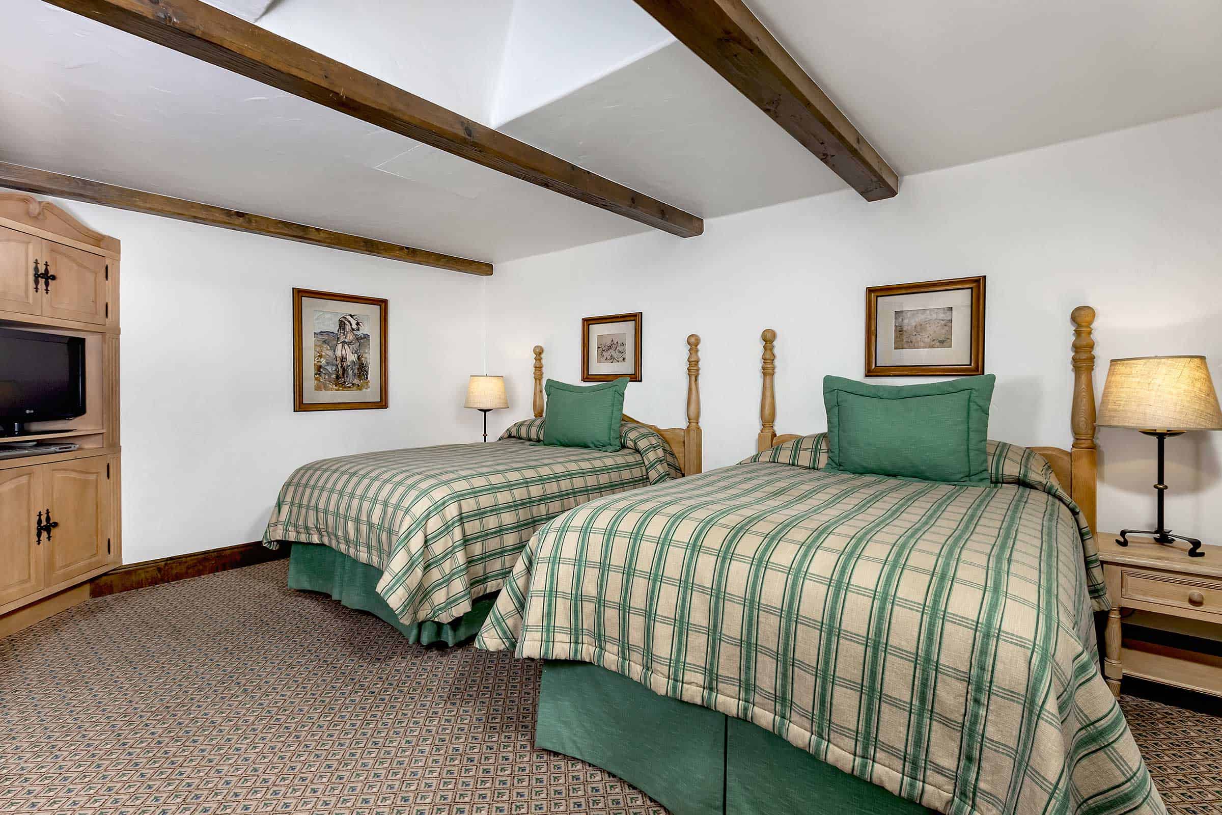 A room with two twin beds, wooden beams on the ceiling, and a plaid bedspread