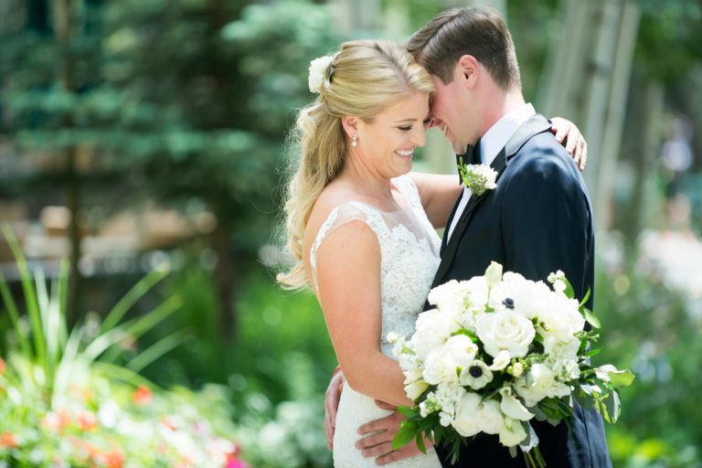 Bride and groom embracing closely outdoors, bride holding a bouquet of flowers