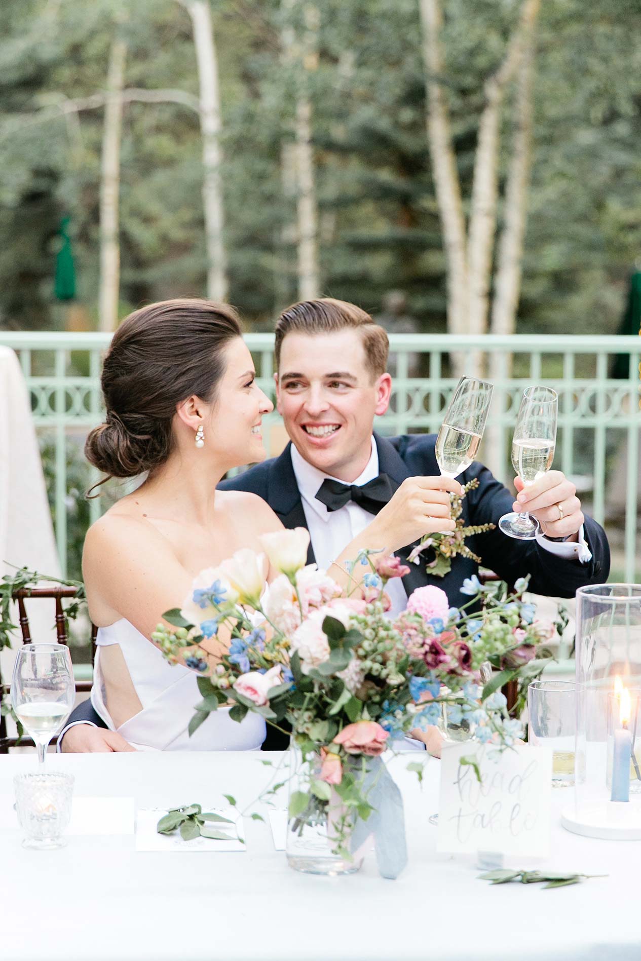 Bride and groom sitting at table, holding champagne glasses