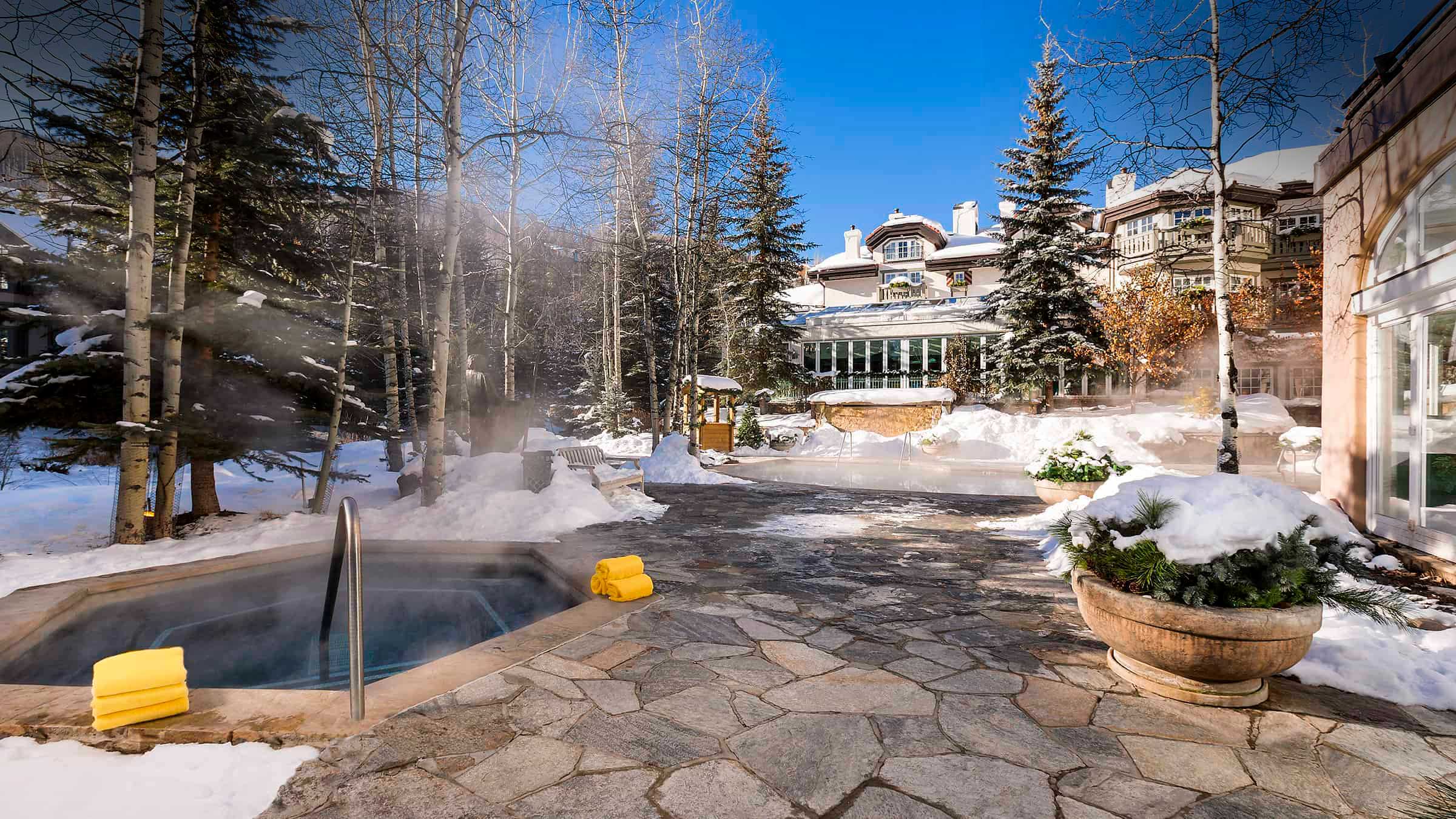 A hot tub in the snow with a large building in the background.
