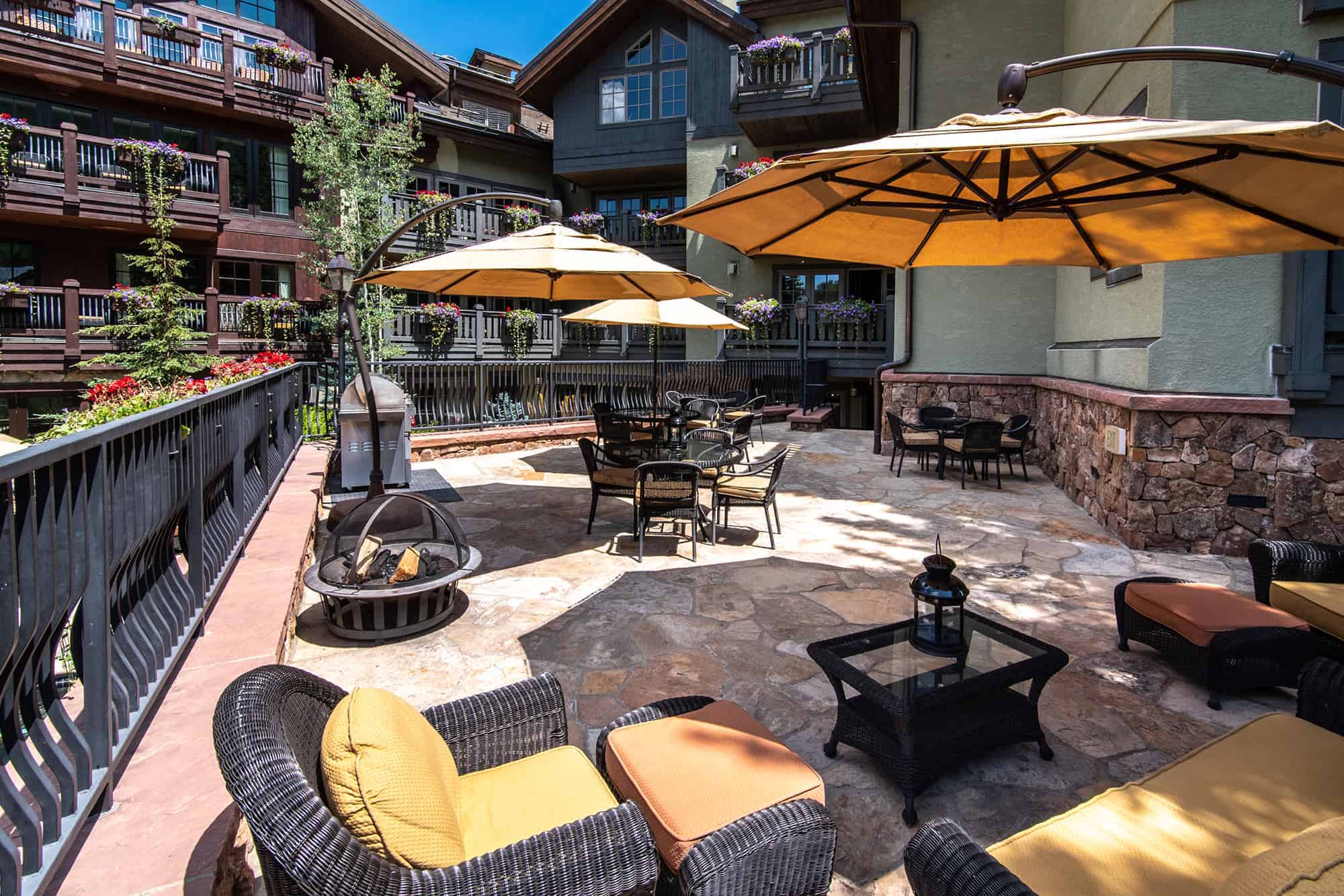A patio area with outdoor furniture, umbrellas, and a fire pit.