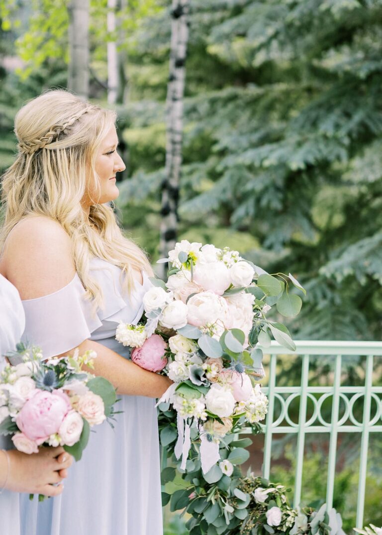 Bridesmaid holding floral bouquet, trees in the background