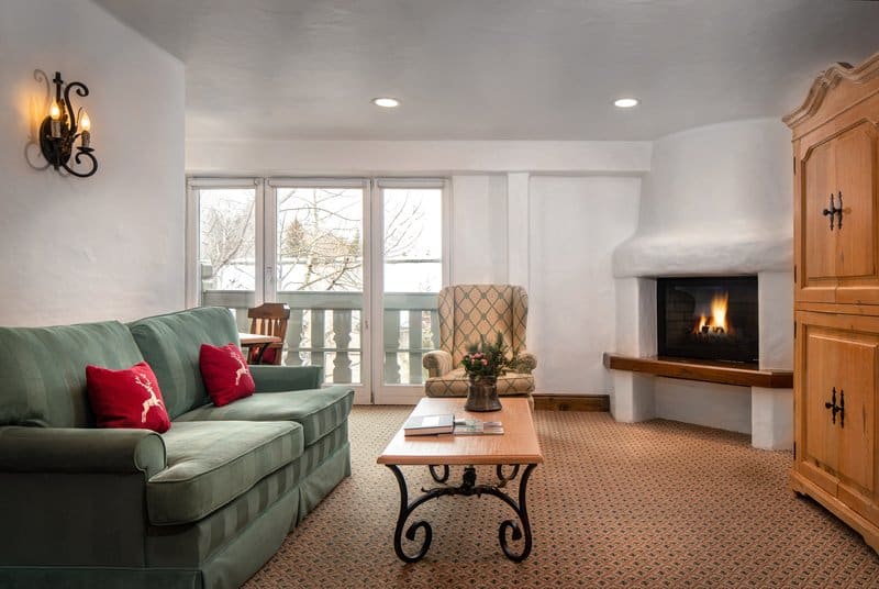 A wide view of a cozy living area with a green sofa, a coffee table, an armchair, and a fireplace.