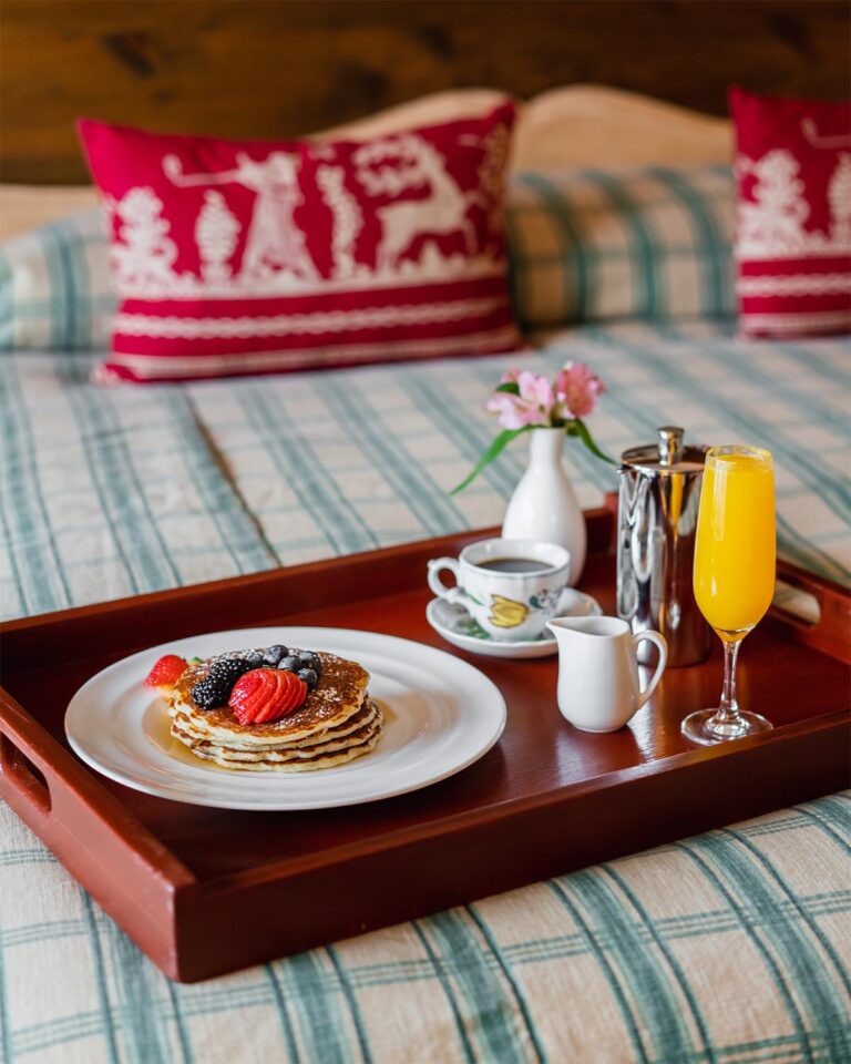 Breakfast tray on bed with plate with pancakes, cup with coffee, and flute with orange juice