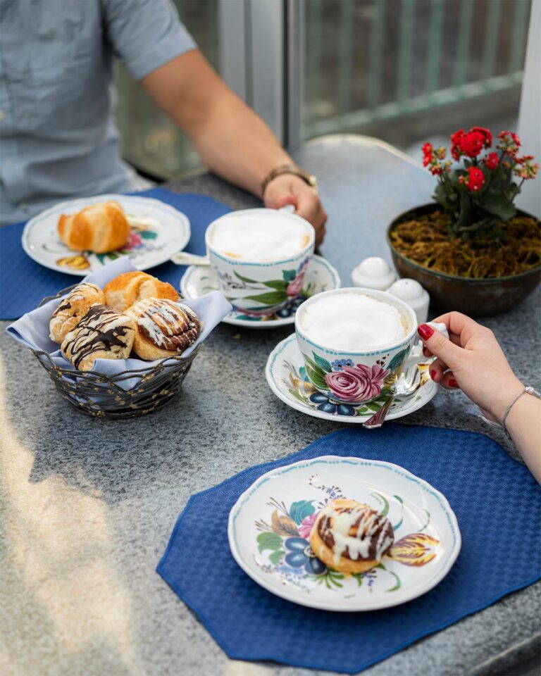 Closeup of table with breakfast pastries, and two people holding coffee cups