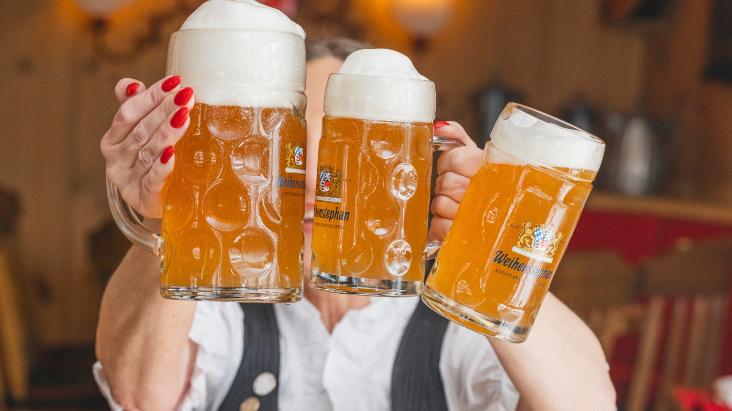 A women dressed in a traditional dirndl holding three steins of beer at Sonnenalp Hotel's Oktoberfest event in Vail, Colorado.