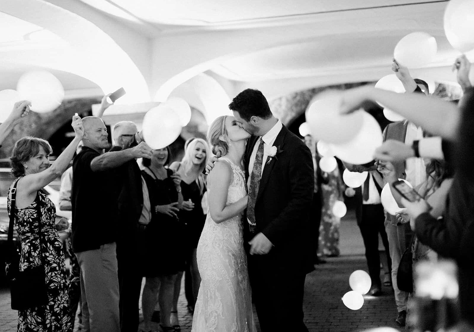 Bride and groom kissing as people stand around and take photos
