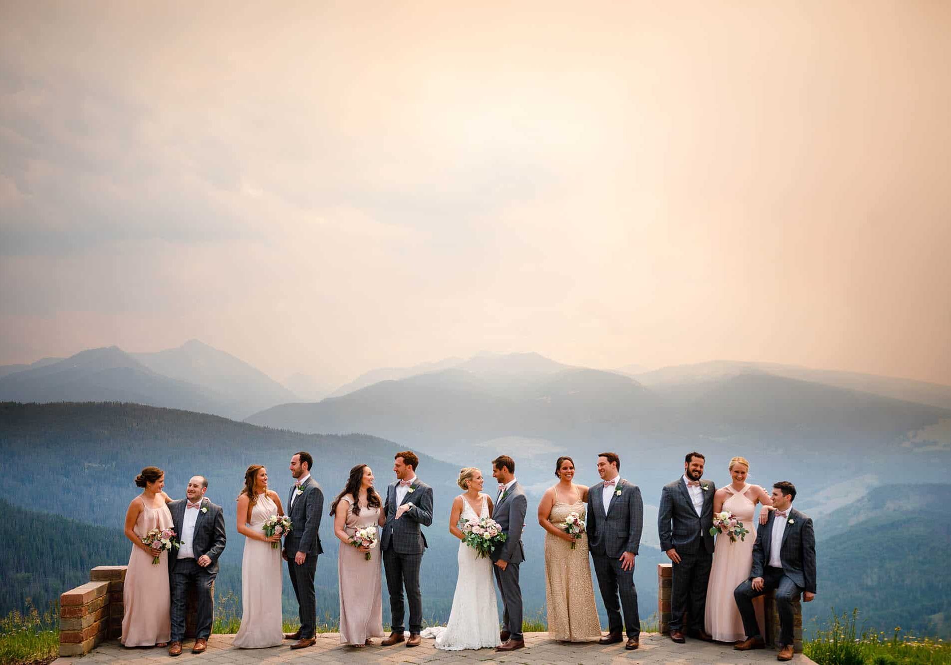 Bride and groom outdoors, in center, bridesmaids and groomsmen on both sides, mountains in the background