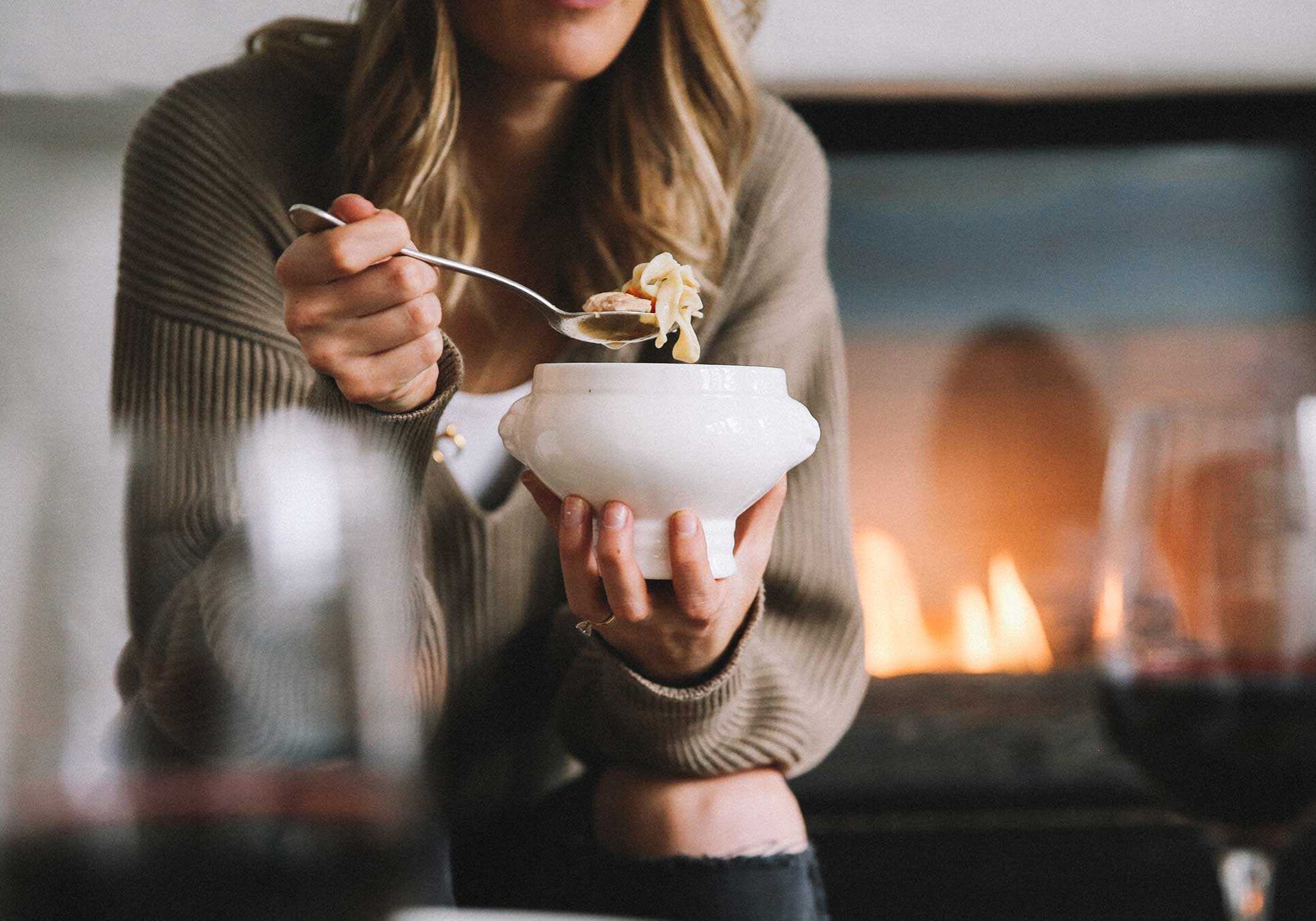 sonnenalp-roomservice-soup Woman eating noodle soup from a bowl, fireplace in the background