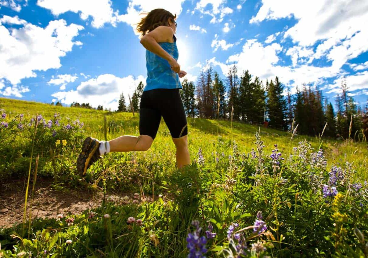 Woman wearing hiking boots, running through a field on a sunny day
