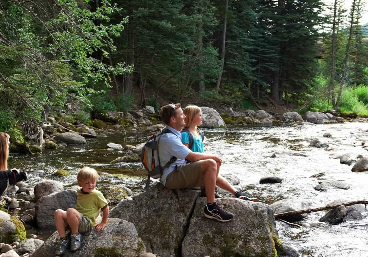 family with dog sitting on rocks on the bank of a creek