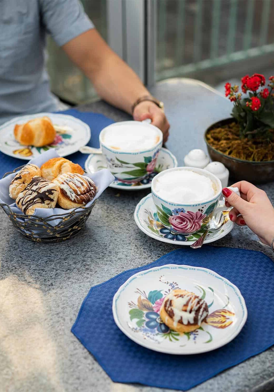Closeup of table with breakfast pastries, and two people holding coffee cups